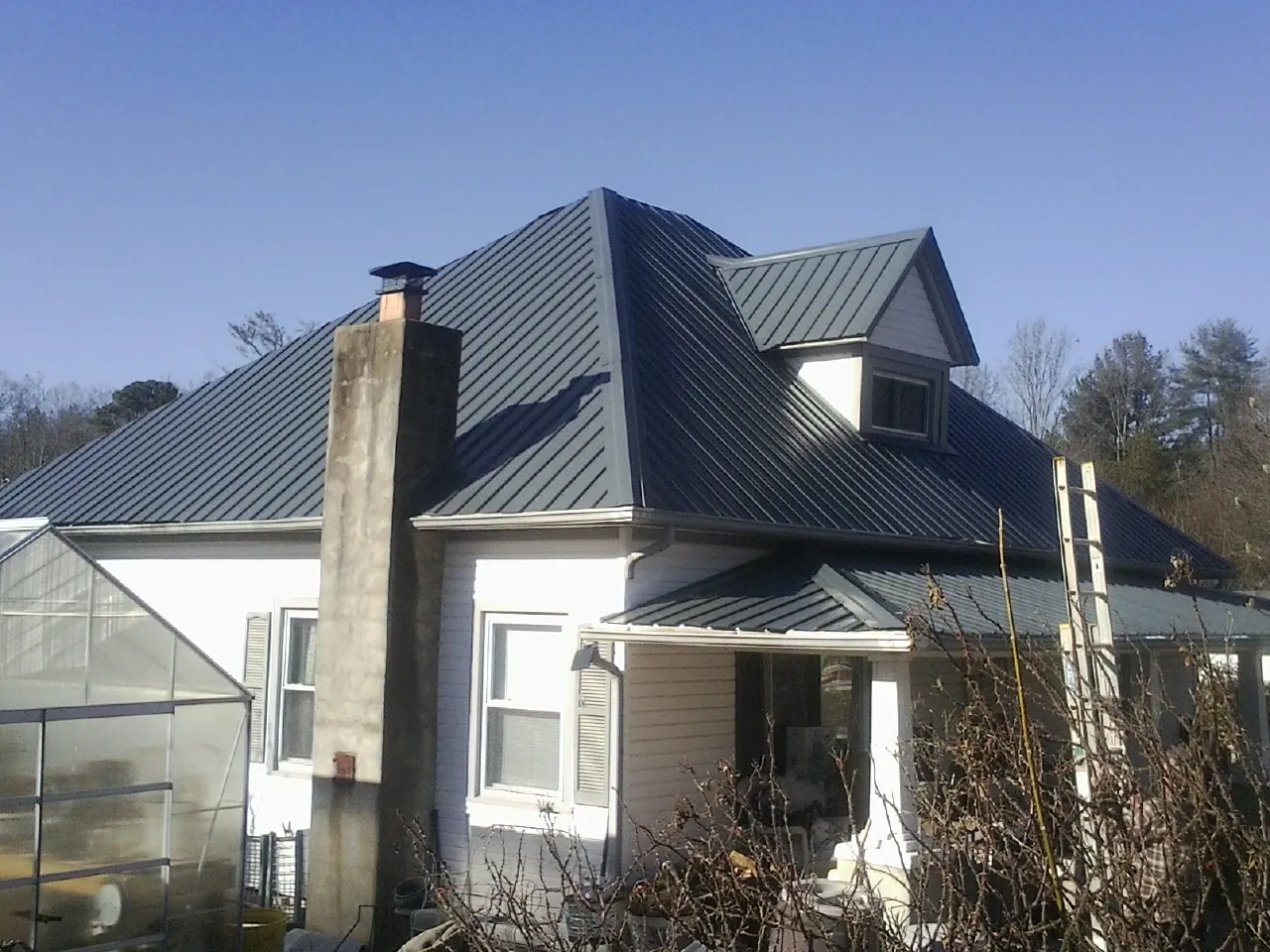 Dark blue standing seam metal roof on a white farmhouse with dormer — Slate & Tile Roof Repair by Roofing Brothers in Maple Hill