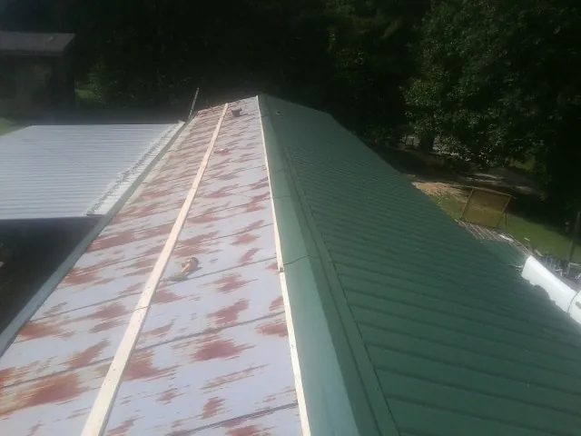 Old rusted panels beside newly installed green metal roofing — Wind Damage Roof Repair by Roofing Brothers in Maple Hill