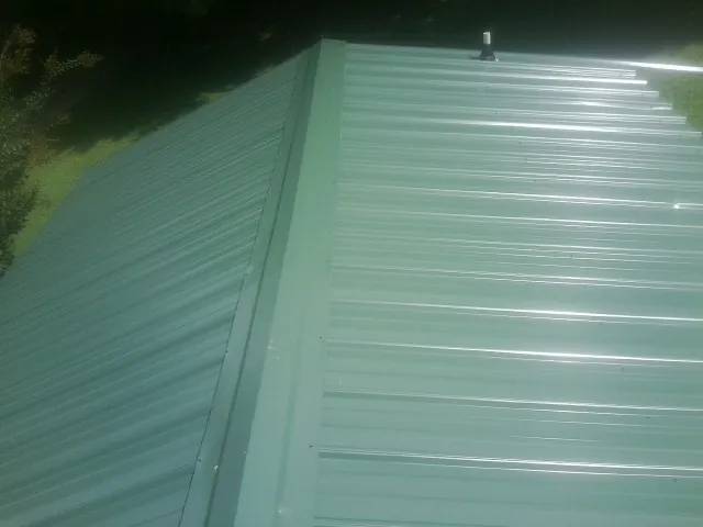New green metal panels meeting at the ridge of a roof — Flat Roof Repair work by our crew in Maple Hill