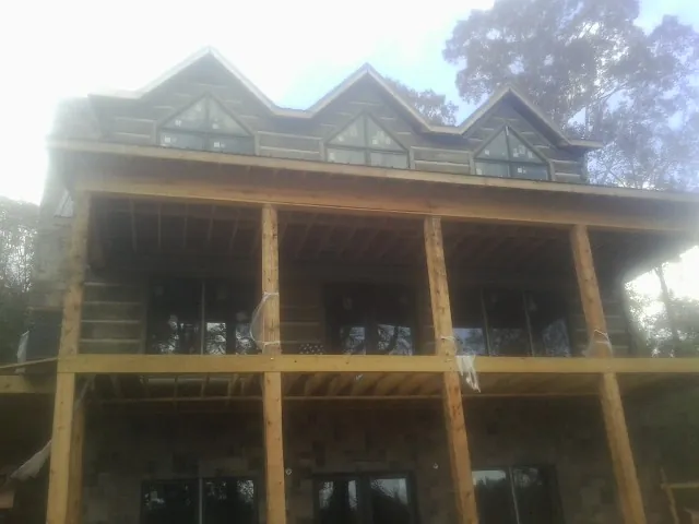Dormers and porch framing on a large log home under construction — Roof Coating work by our crew in Maple Hill