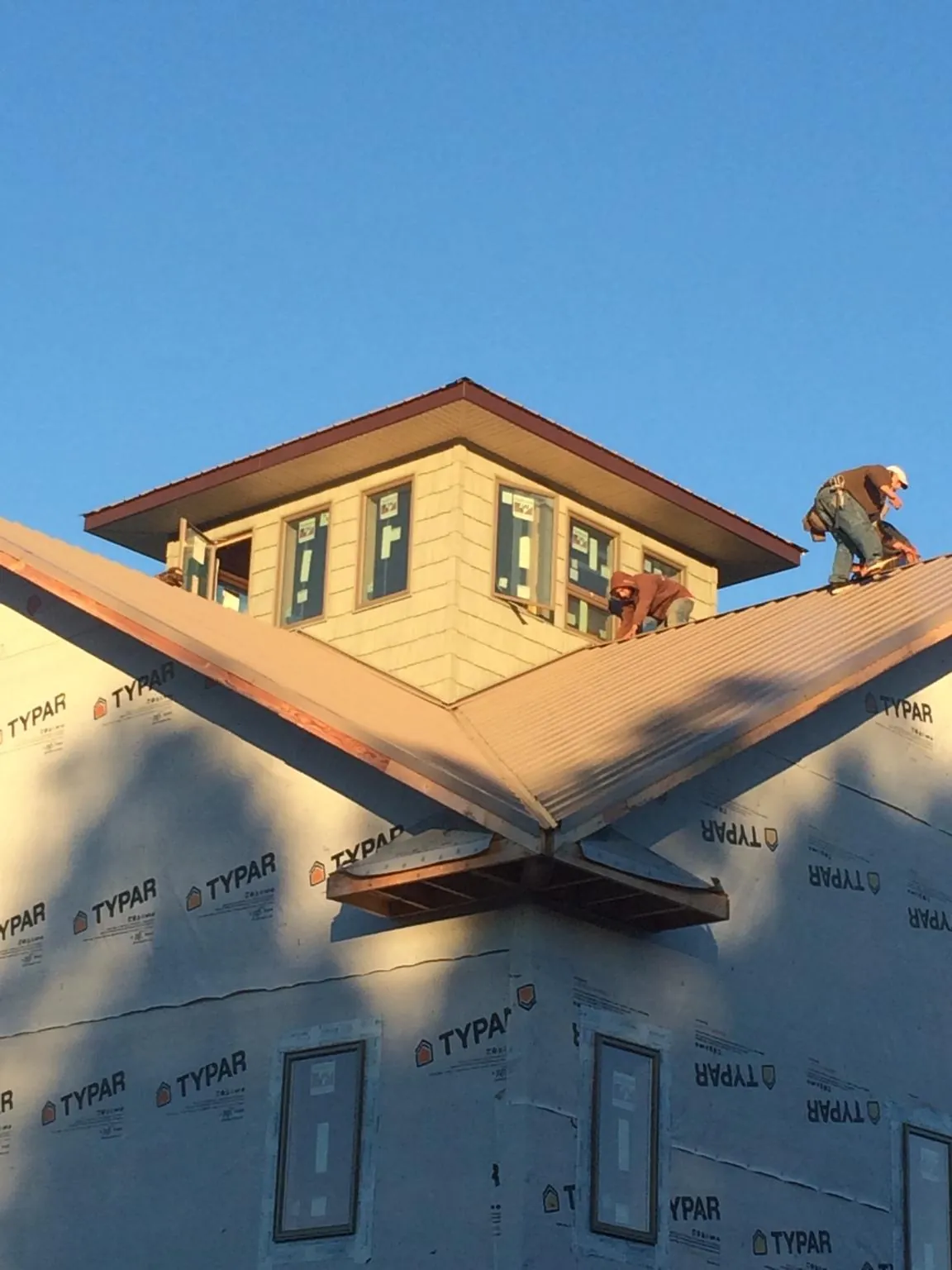 Roofers working around a rooftop cupola on a new metal roof at sunset — Roof Waterproofing in Maple Hill by Roofing Brothers